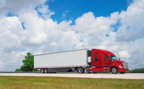 Red semi-truck driving down a lonely highway during the day
