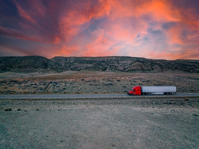 Semi truck drives on a desert highway at sunset